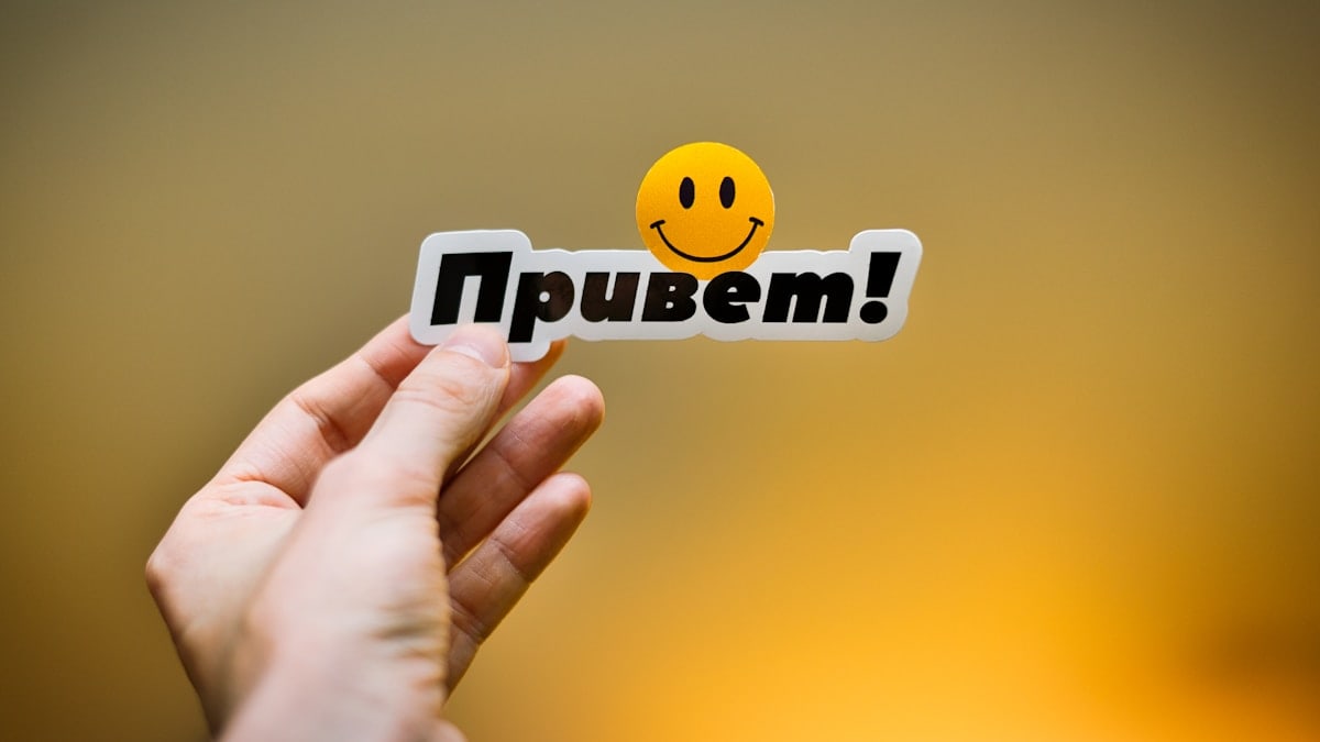 Hand holding a sticker with "привет!" and a smiley face.